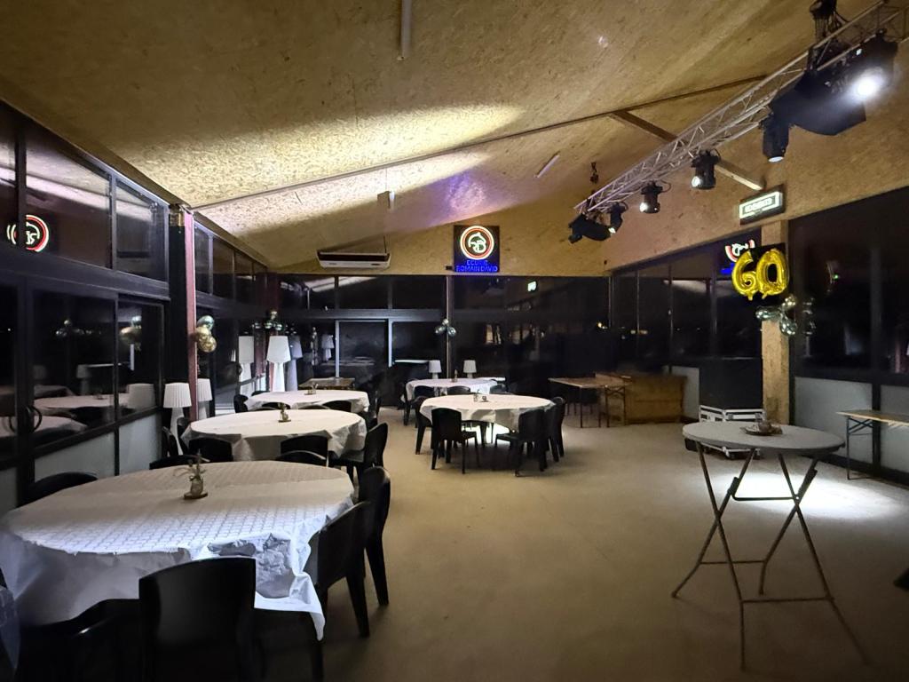 Intérieur d'un restaurant avec des tables rondes, des chaises noires et une décoration d'anniversaire avec des ballons dorés.